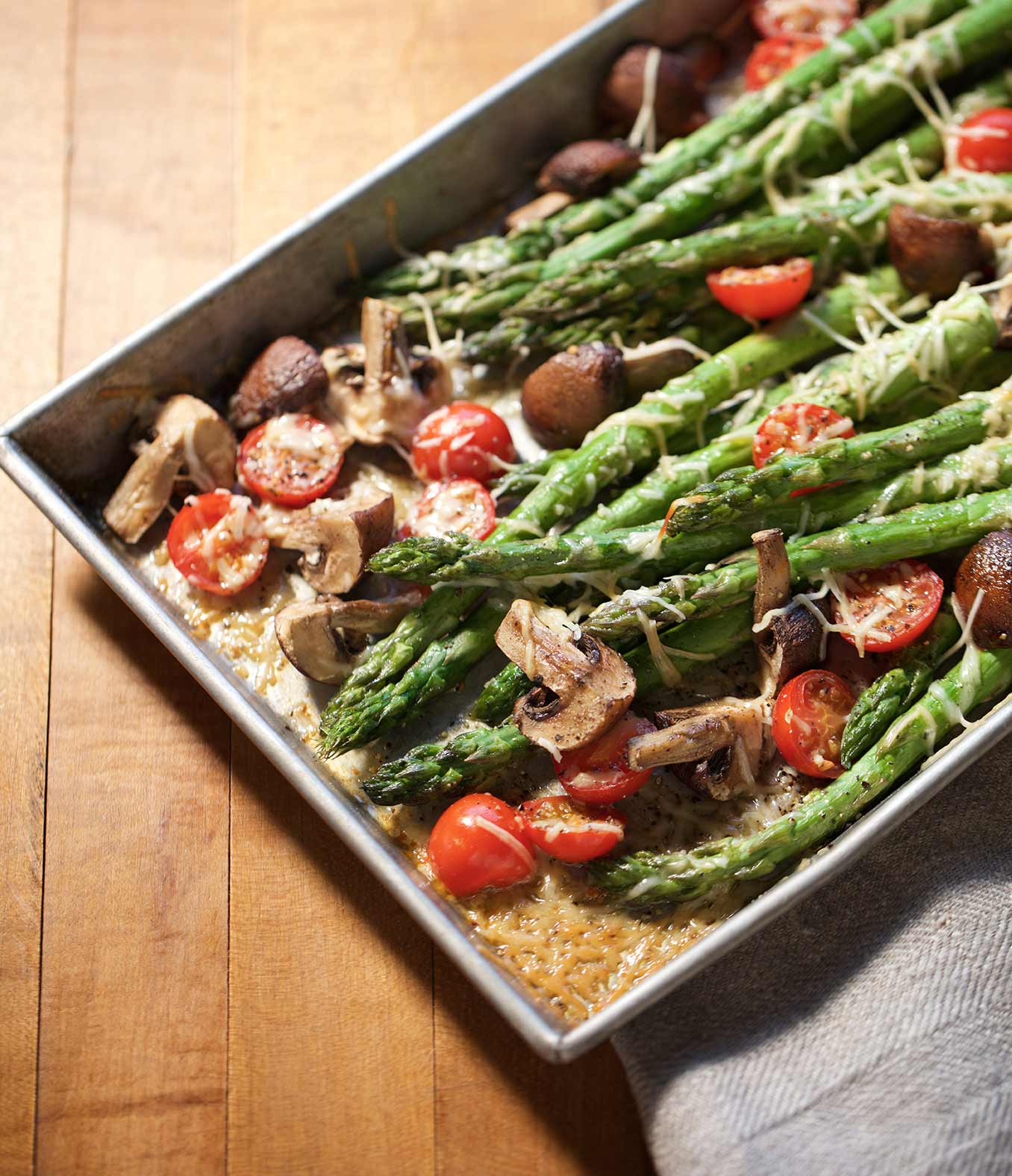 Asparagus with mushrooms, cherry tomatoes and parmesan cheese on a sheet pan.